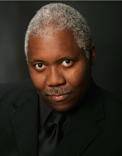 Head and shoulders of an older African American man with short, gray hair in all-black formal wear